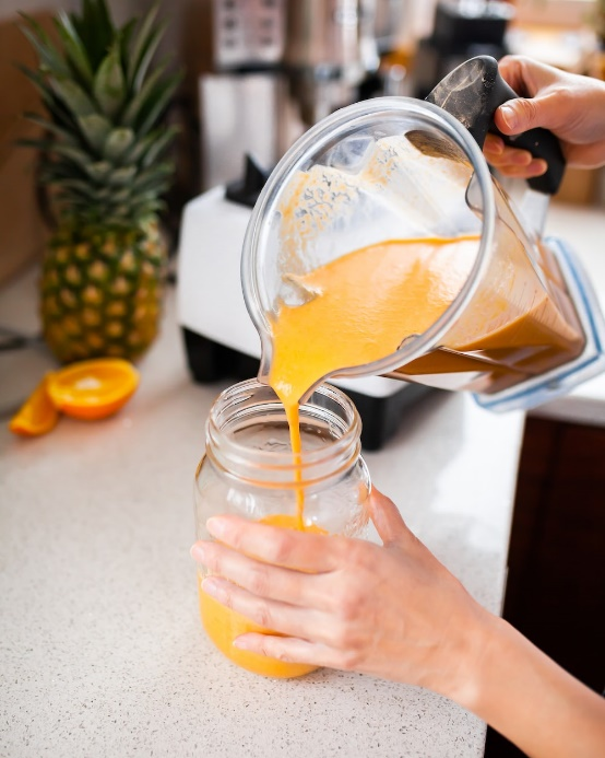  A person pouring mango smoothie into a glass